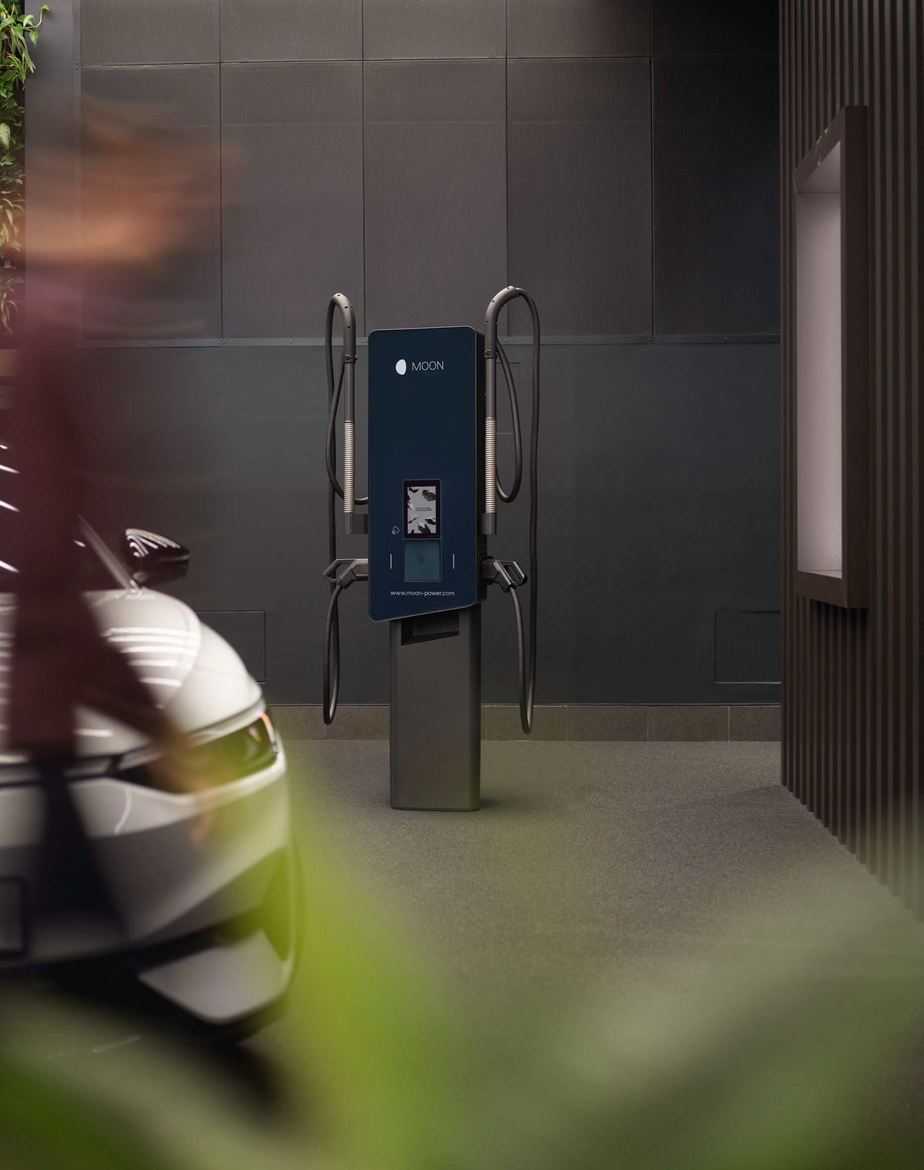 Зарядна станция пред сива стена с кола на преден план