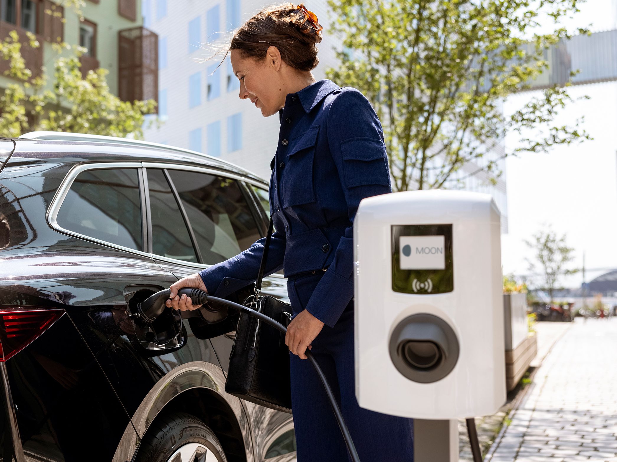 Жена, която поставя кабел за зареждане към автомобила си от стенна зарядна станция, която е на преден план