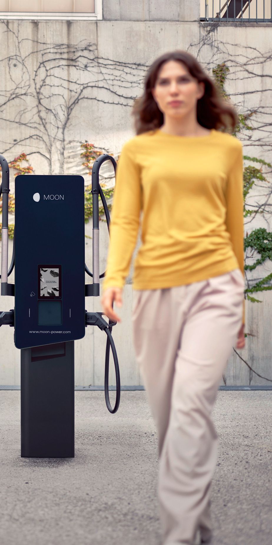 Жена минава пред зарядна станция с кола на заден план