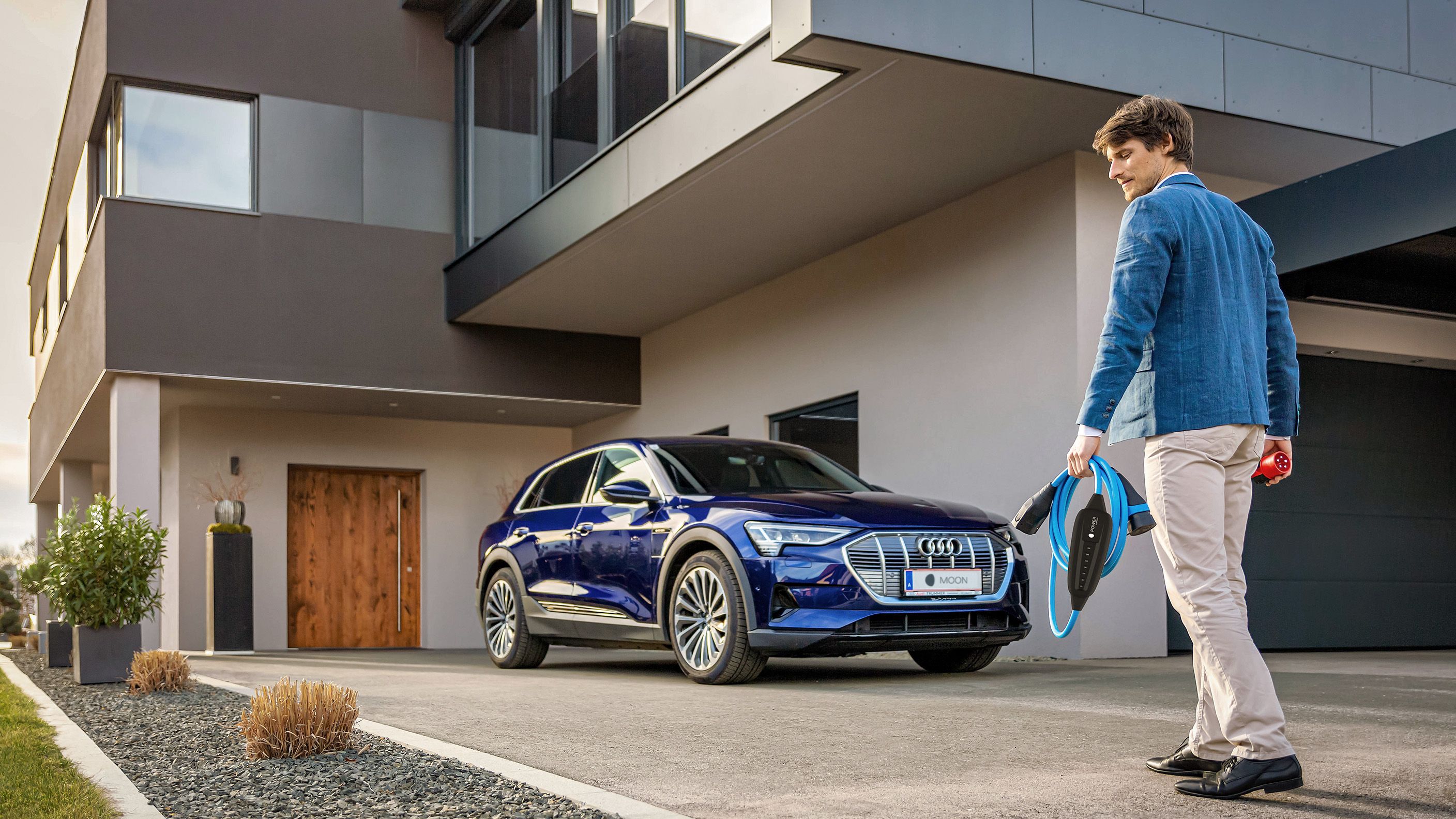 Мъж върви към кола близо до къща с кабел в ръка