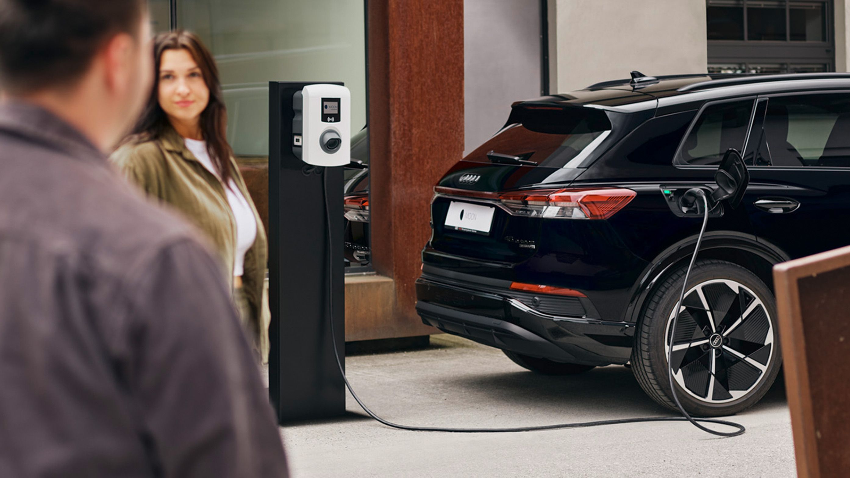 Кола се зарежда на зарядна станция с двама души на преден план