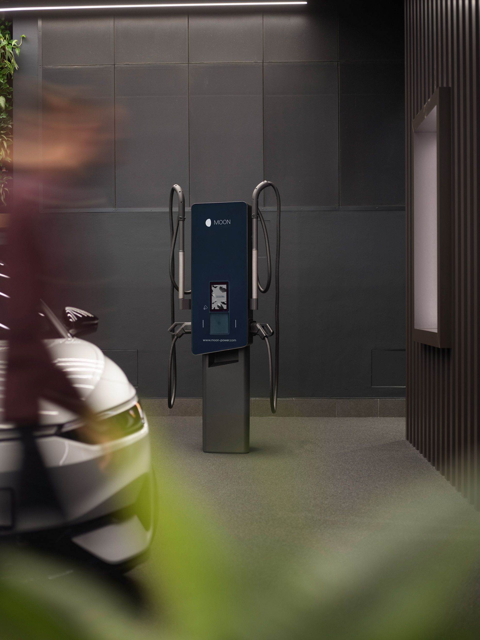 Зарядна станция в стая със сиви стени и кола на преден план